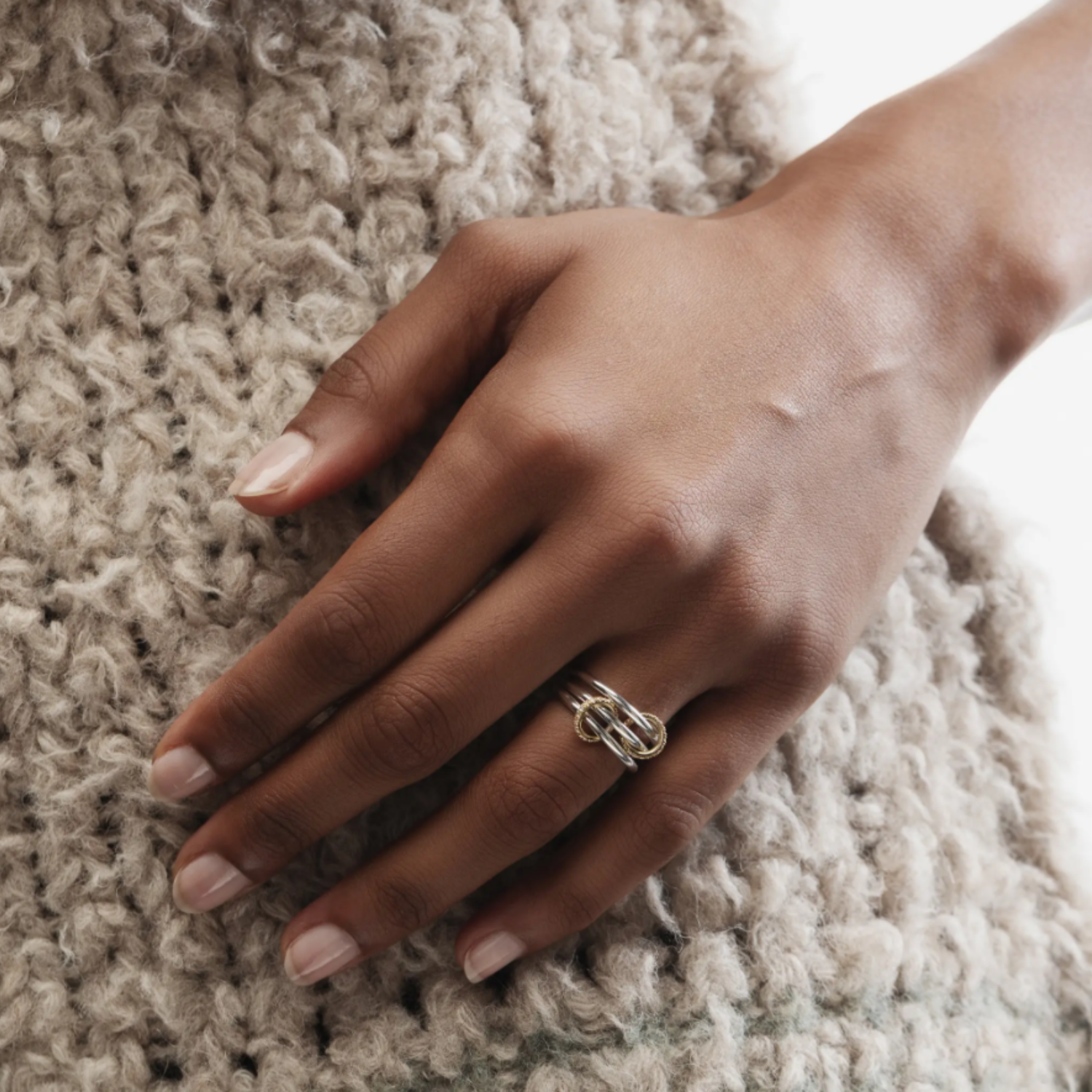 Hand wearing a ring on a textured beige surface