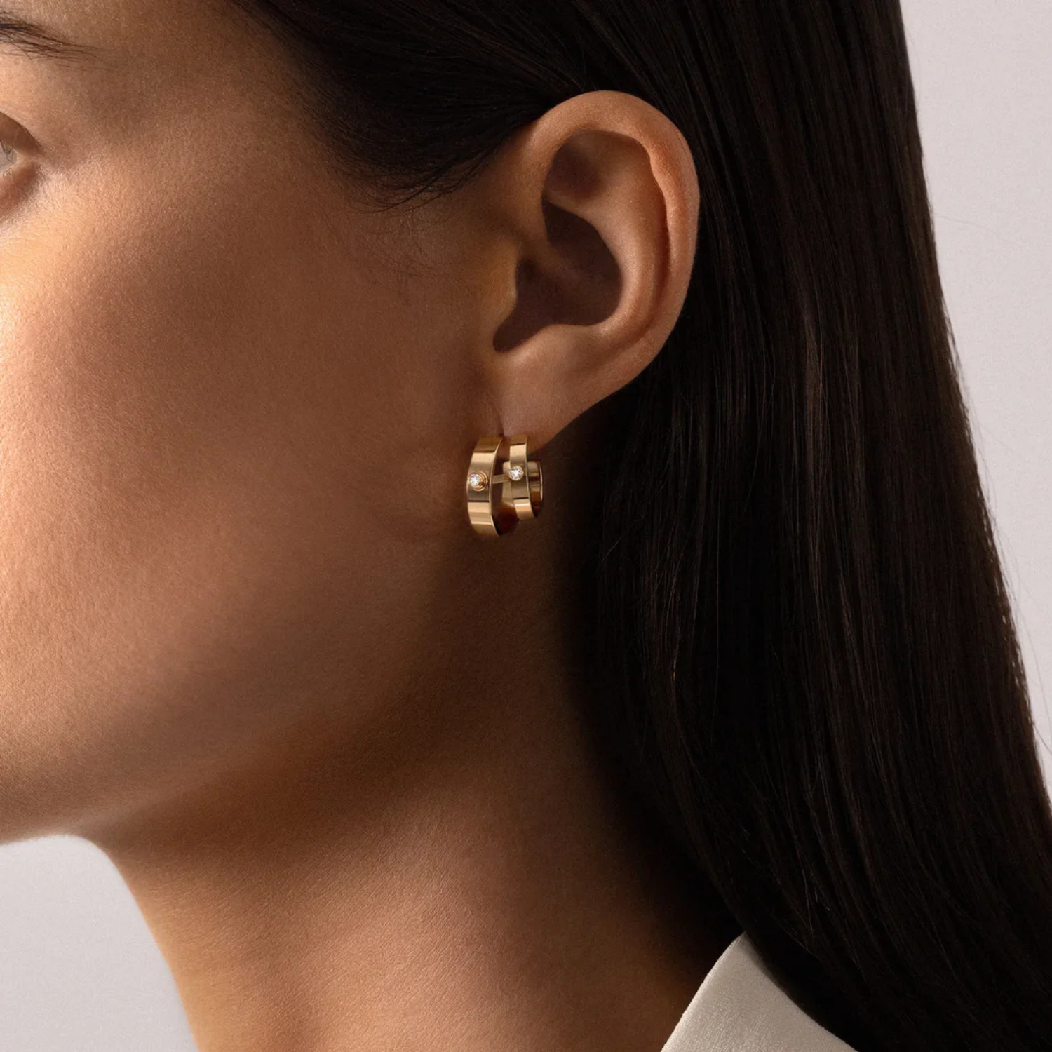 Close-up of a person wearing gold hoop earrings with a neutral background