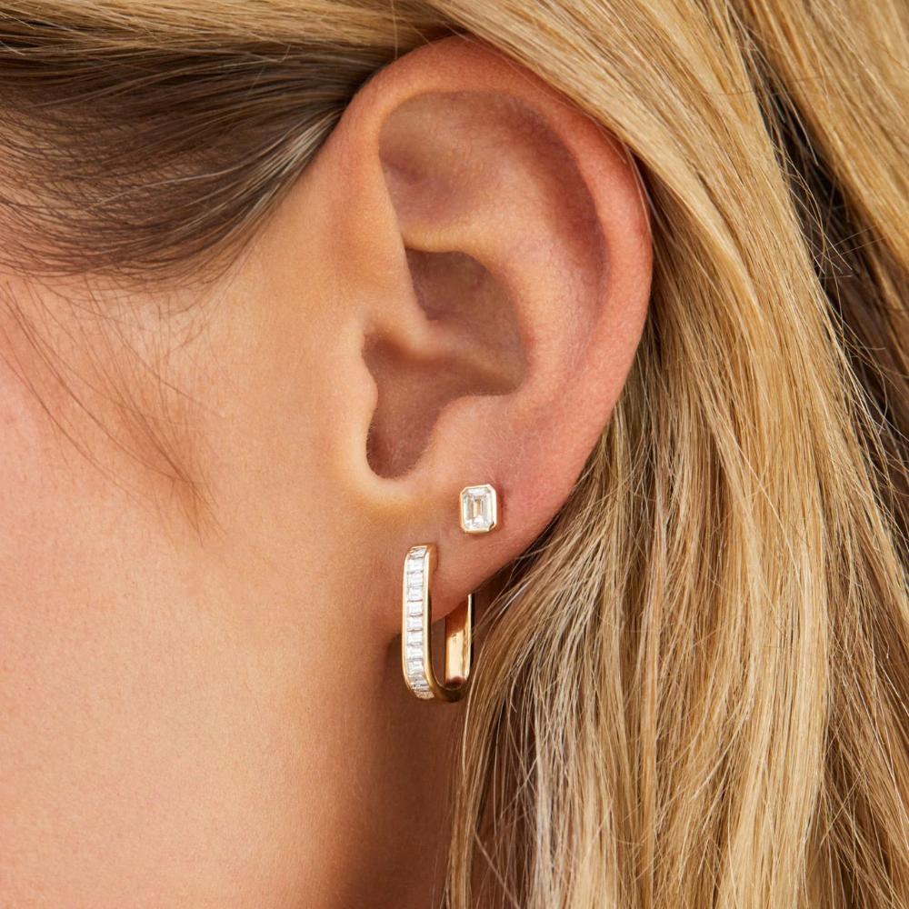 Close-up of an ear wearing gold hoop earrings with a blurred background