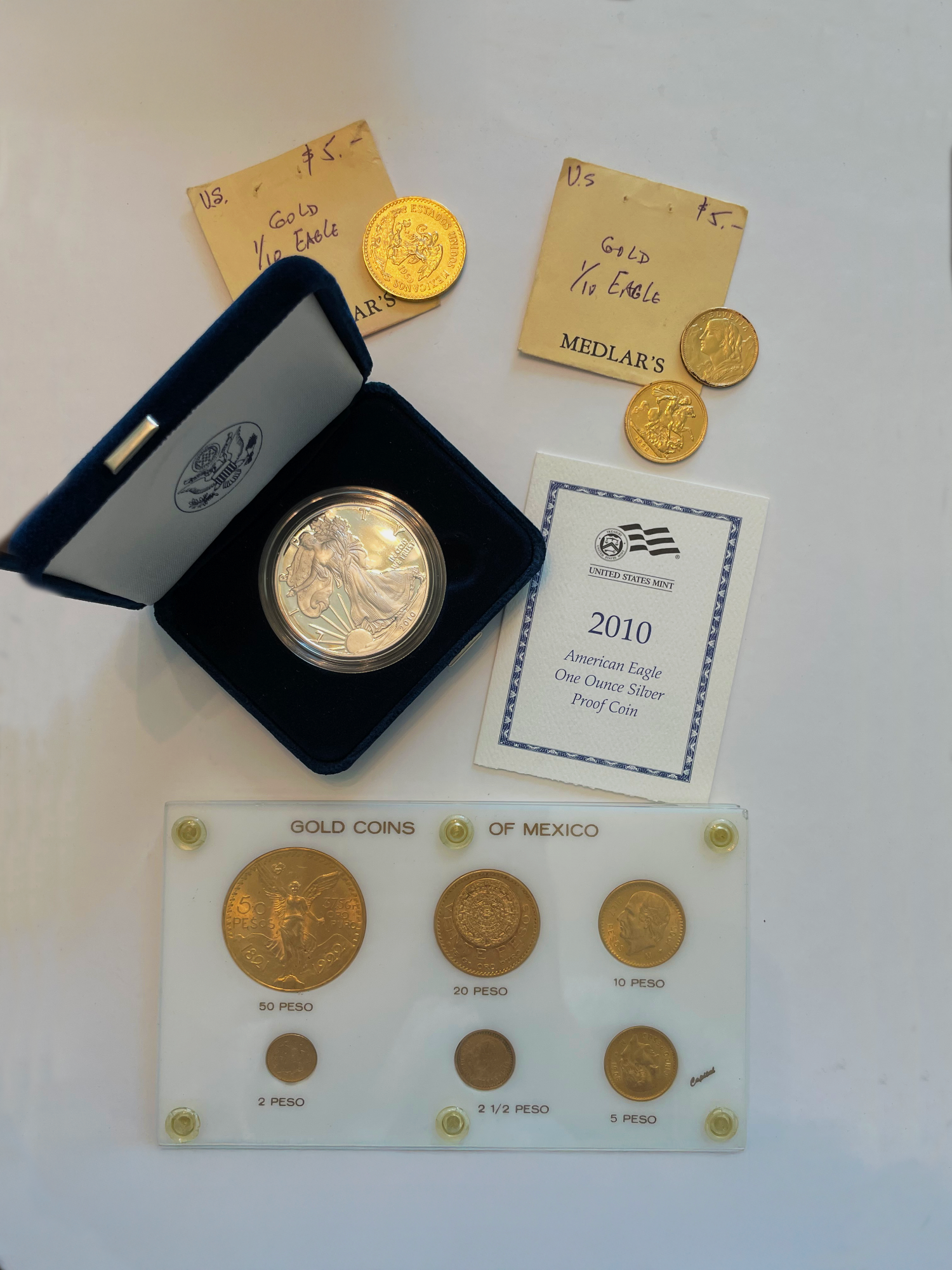 Gold coins including a 2010 American Eagle silver proof coin, displayed with an educational card about Mexican gold coins.