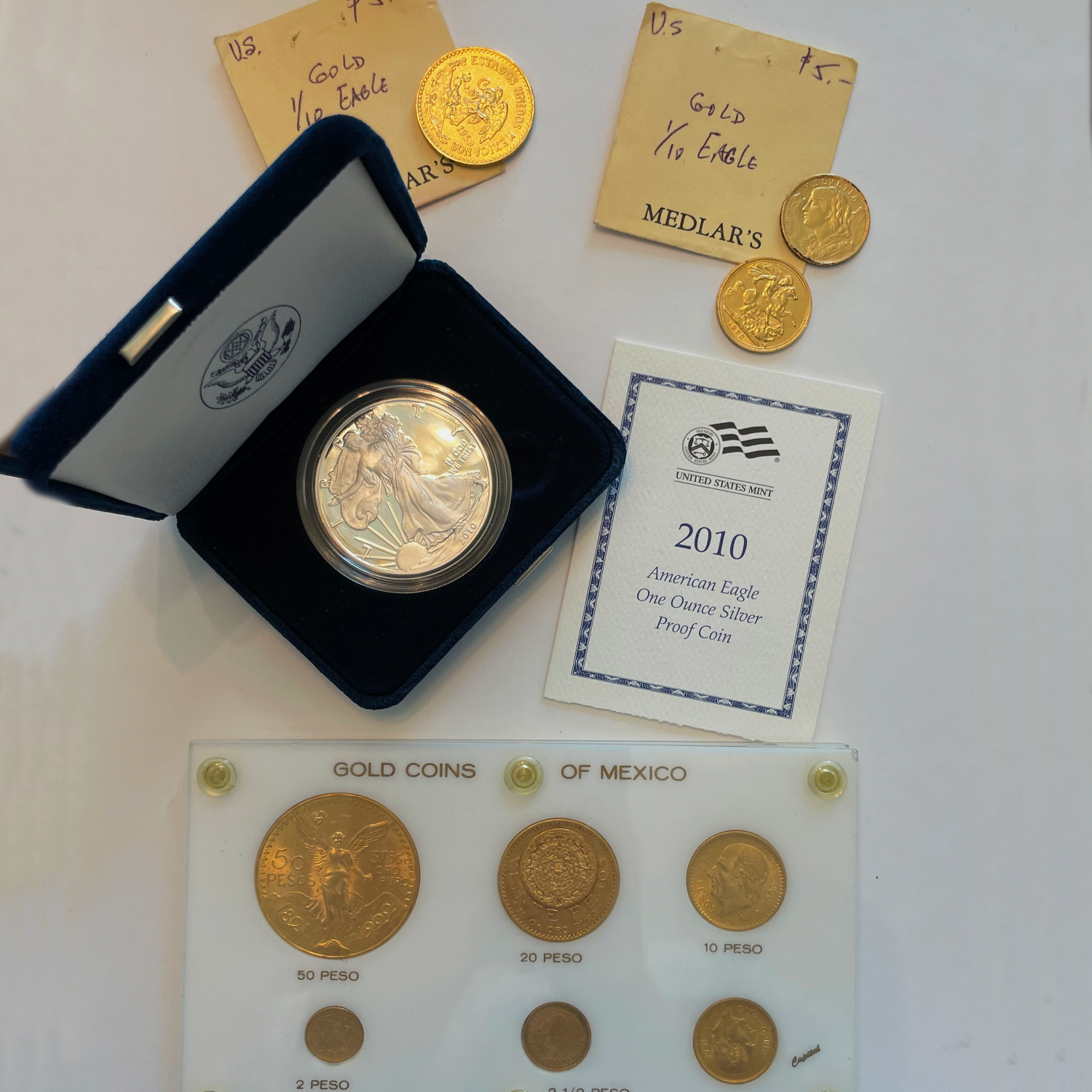 Gold coins including a 2010 American Eagle silver proof coin, displayed with labels and a display case.