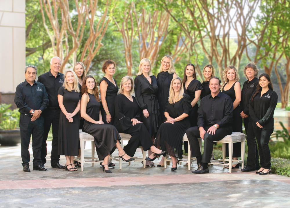 Group of people in formal attire posing outdoors with trees in the background