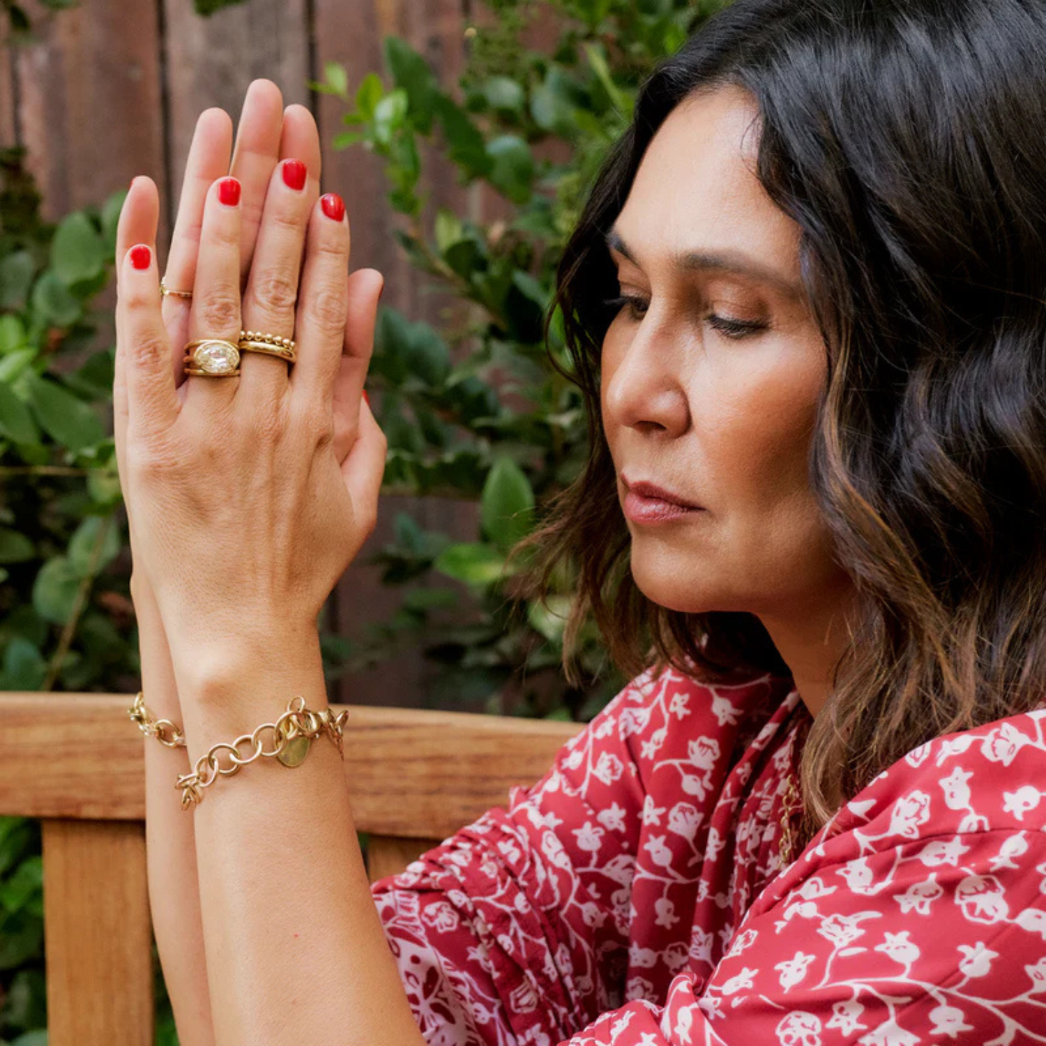 Woman wearing gold jewelry with red nail polish, sitting outdoors.